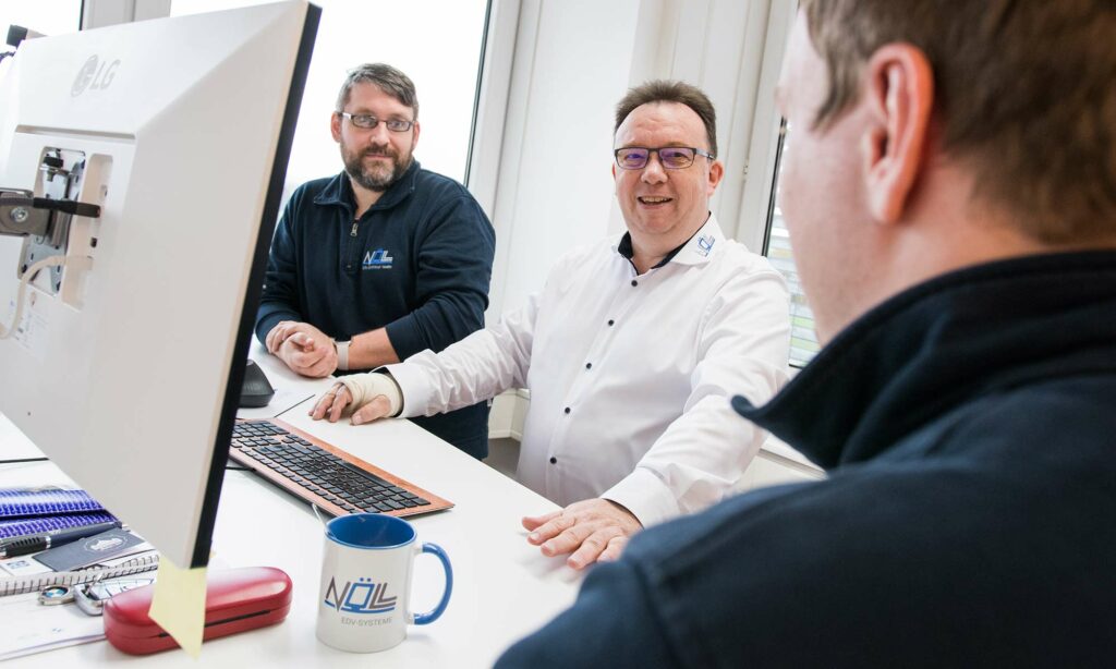 Zu sehen sind Dennis, Andreas und Marvin am Schreibtisch im Büro von Nöll EDV-Systeme GmbH.